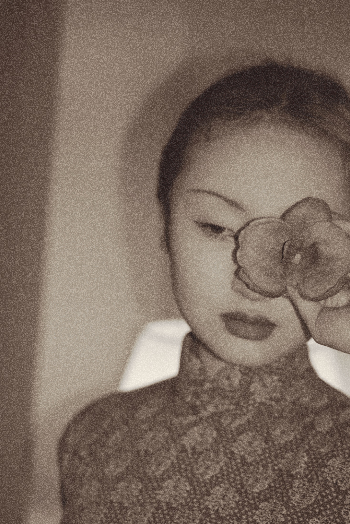 A sepia portrait with a flower held over one eye